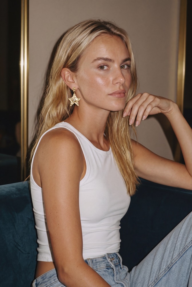 AVA Atelier campaign image: a woman wearing the star earring, seated on a blue velvet sofa